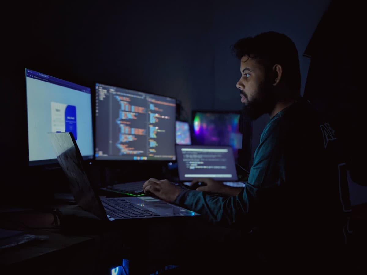 Desenvolvedor programando à noite em ambiente com múltiplos monitores exibindo código