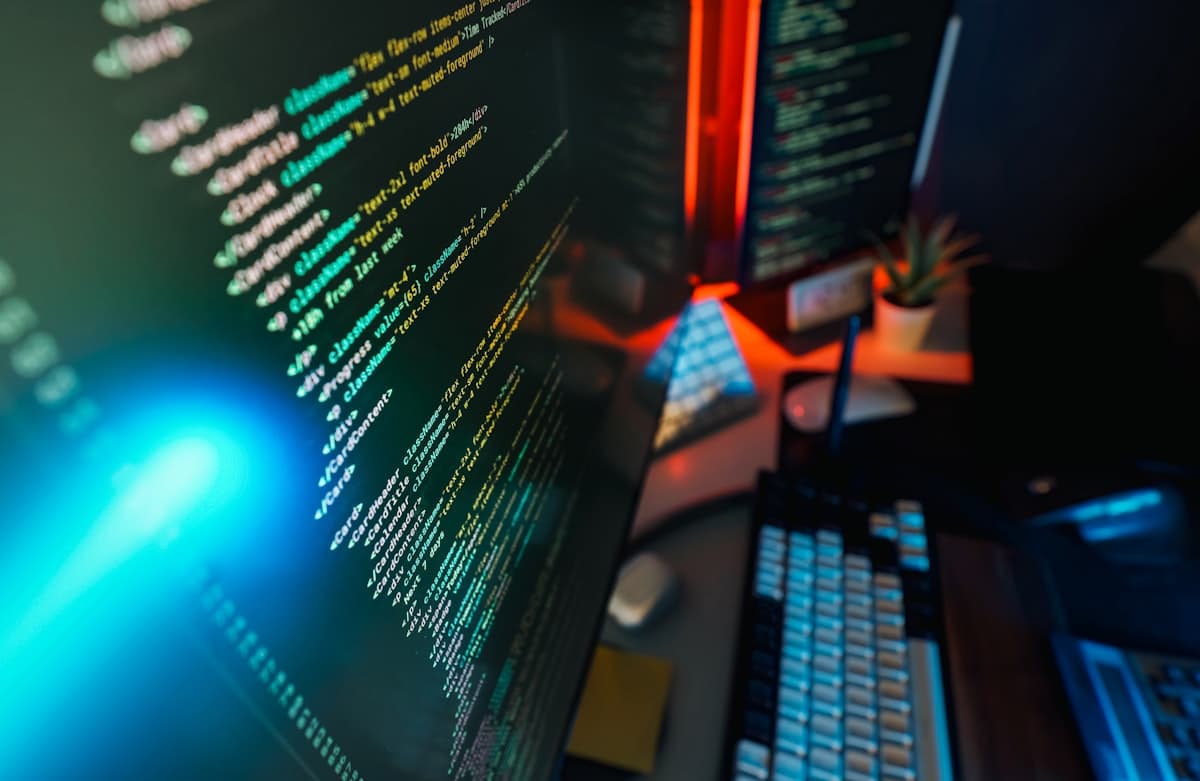 Tela de computador exibindo código colorido com iluminação neon azul e vermelha — ambiente profissional de desenvolvimento de software