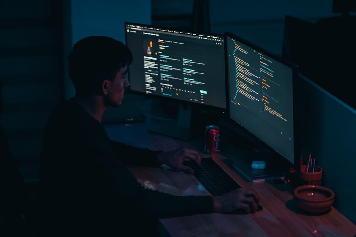 Desenvolvedor focado em frente a múltiplos monitores com código em tela escura
