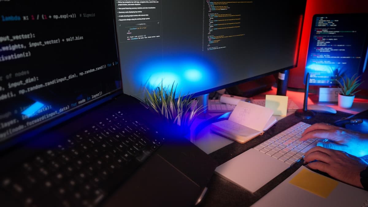 Programador trabalhando em setup com múltiplos monitores exibindo código e interfaces de desenvolvimento